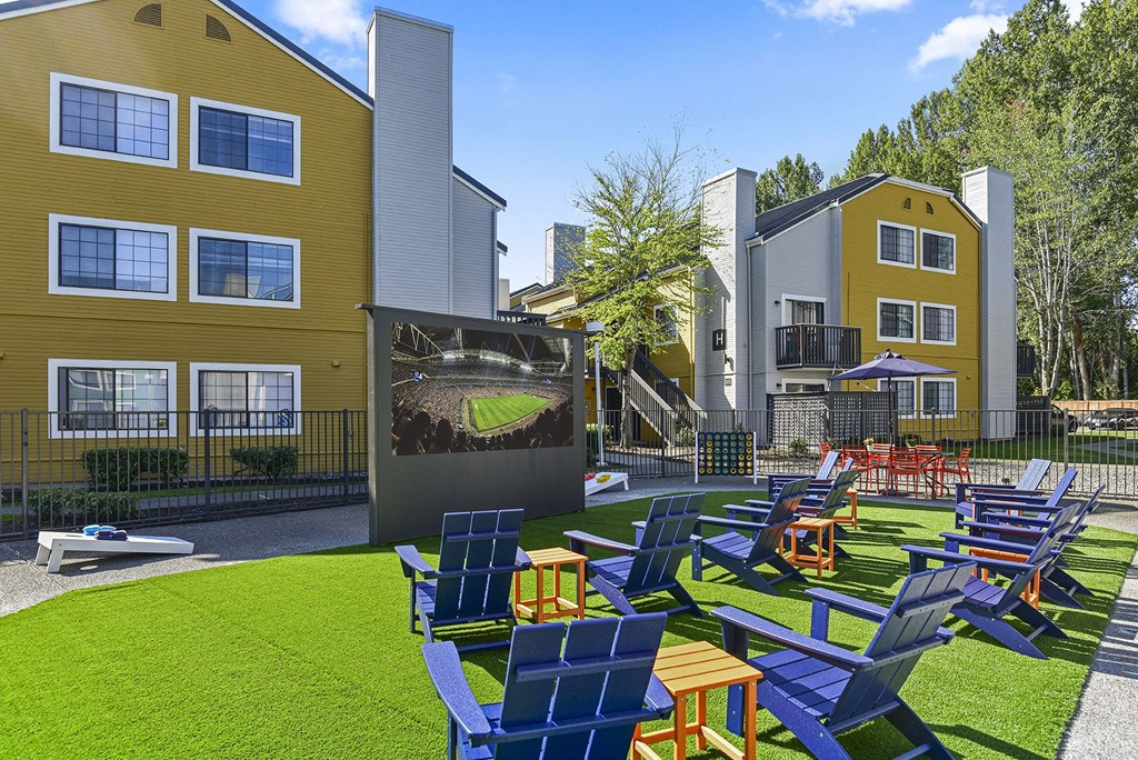 an outdoor lounge area with chairs and a movie screen in front of buildings