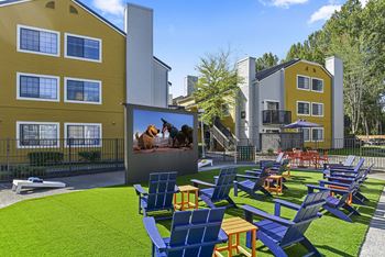 an outdoor lounge area with chairs and a video screen in front of apartment buildings