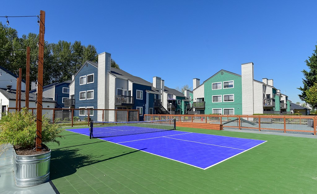 a blue and green tennis court with apartments in the background