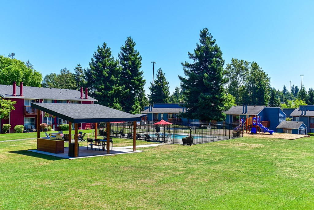 a large grassy area with a playground and buildings in the background