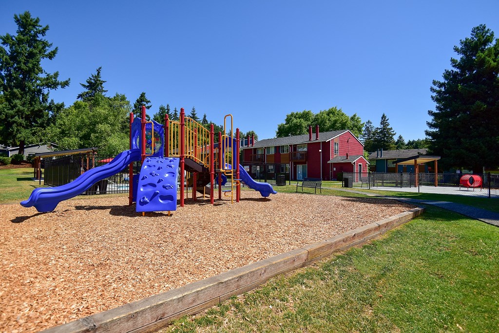 a playground with a blue slide and a red building in the background