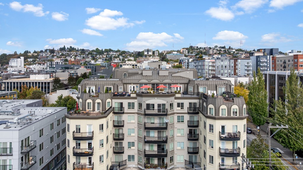 A large apartment building with a balcony on the second floor overlooks a cityscape.