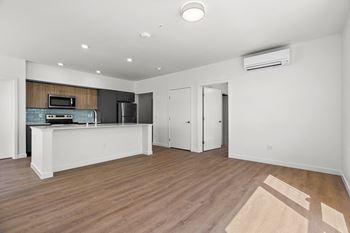 an empty living room with a kitchen and wood flooring
