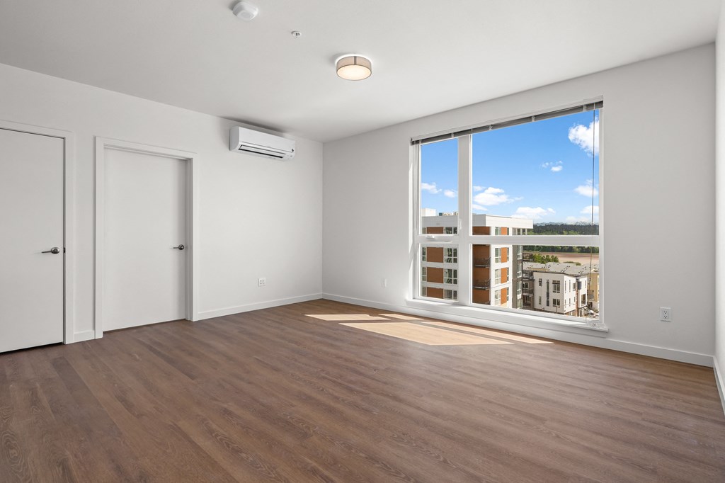 an empty living room with a large window and wood flooring