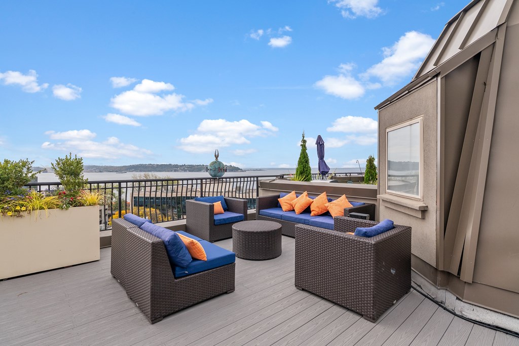 A patio with a couch, table, and chairs overlooking a body of water.