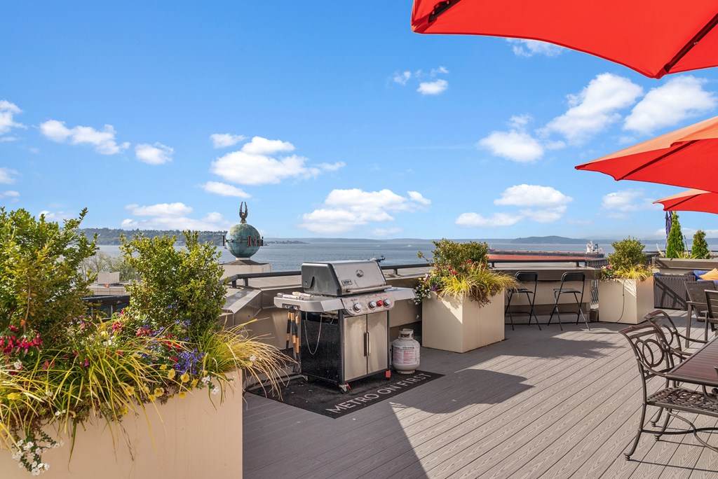 A patio with red umbrellas and a grill overlooking the water.
