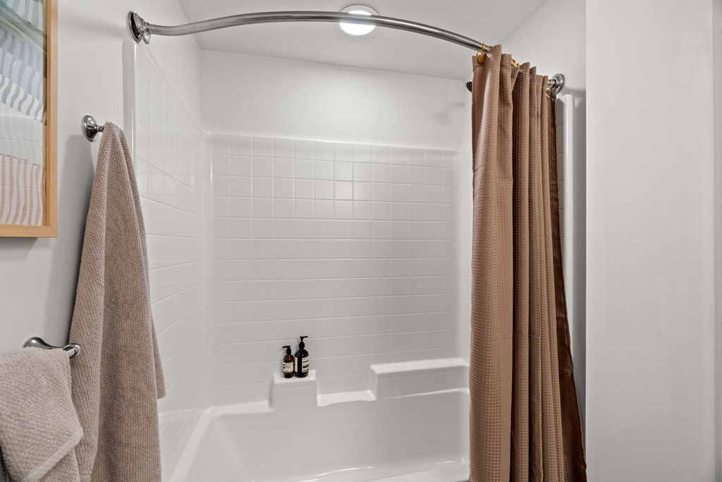 A white shower with white tiles and light brown shower curtain