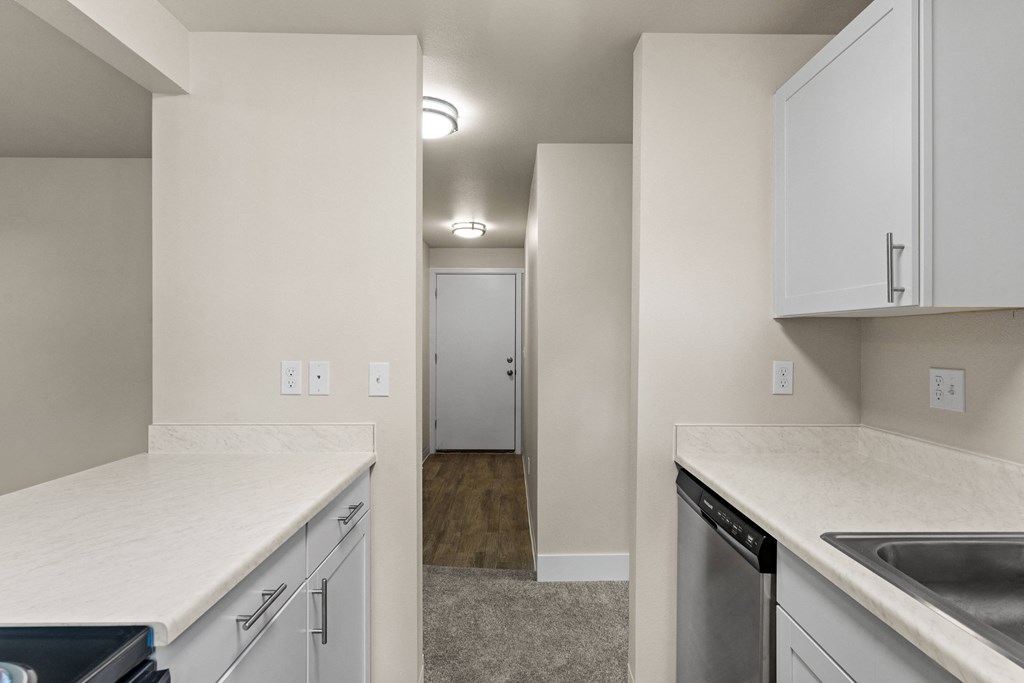an empty kitchen with white countertops and white cabinets and a door to a hallway