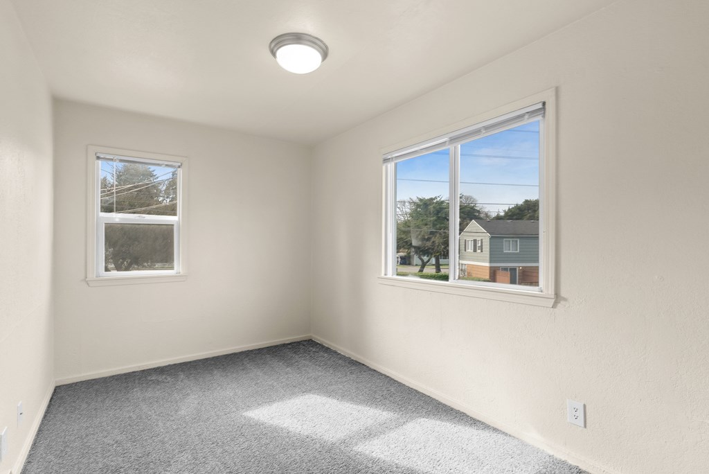 A room with a carpeted floor, two windows, and a ceiling light fixture.