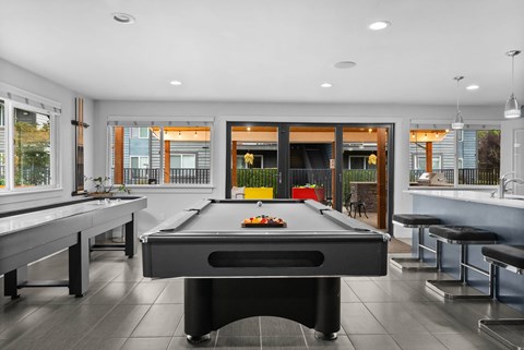 A pool table is in the middle of a room with a bar and a balcony.