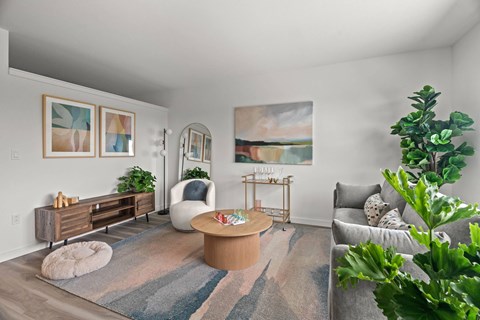 A living room with a grey couch, a white chair, a wooden coffee table, and a painting on the wall.
