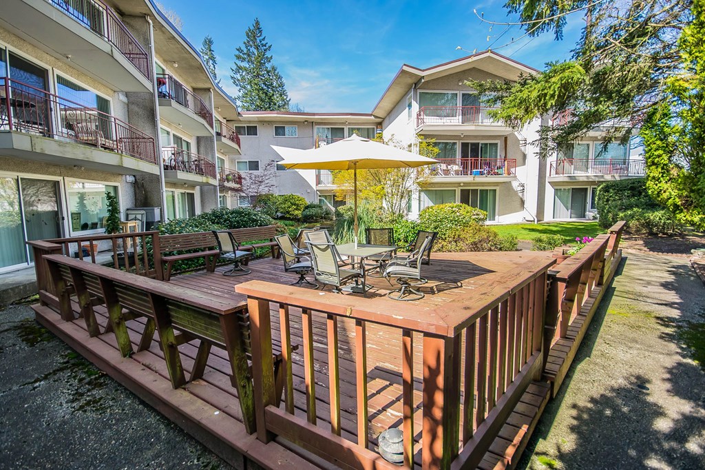 A wooden deck with chairs and a table is in the foreground of a sunny day.