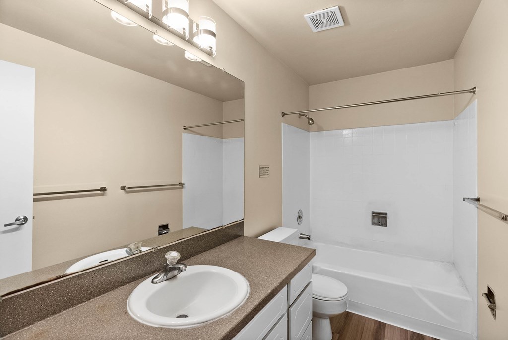 A bathroom with a sink, mirror, toilet and bathtub.