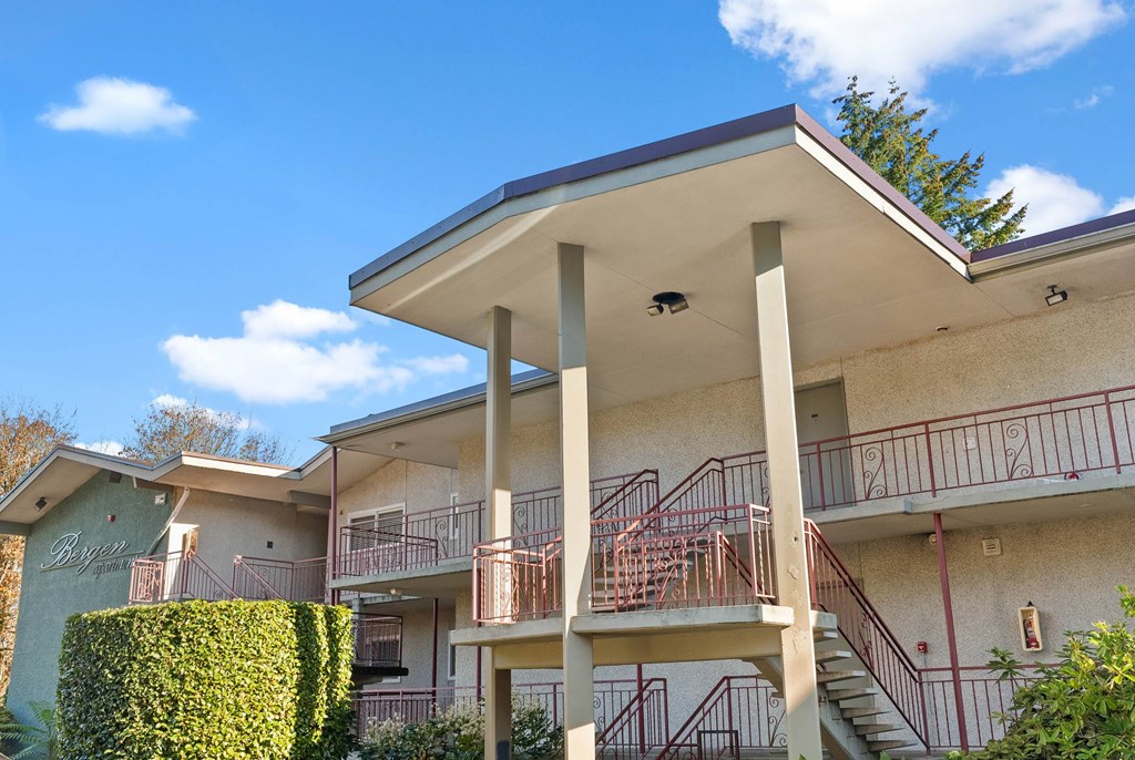 A building with a balcony and stairs is surrounded by greenery.