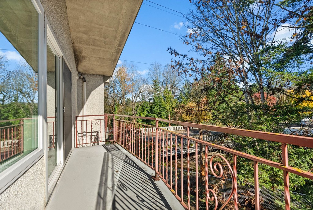 A balcony with a metal railing and a view of trees and a blue sky.
