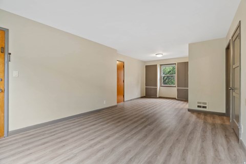 A room with wooden flooring and a window with a view of trees.