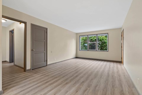 A room with a wooden floor and a window showing greenery outside.