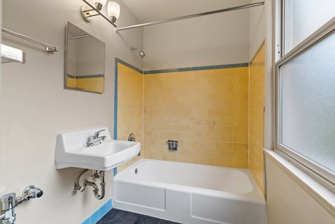 A white sink is mounted on a wall next to a bathtub in a bathroom.
