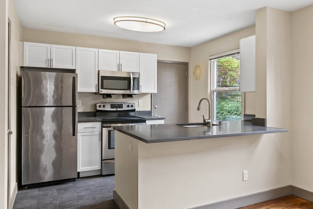 A kitchen with a refrigerator, microwave, oven, and sink.