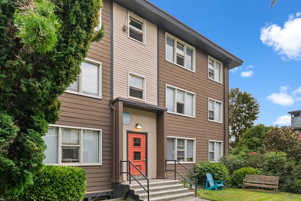 A brown house with a red door and a green chair in front.