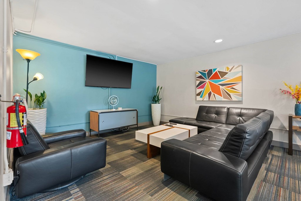 A black leather couch sits in a room with a blue wall and a television.