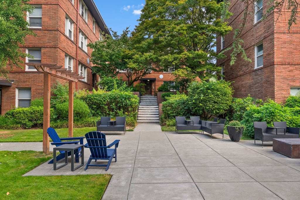 A courtyard with a concrete floor, blue chairs and tables, and a brick building in the background.