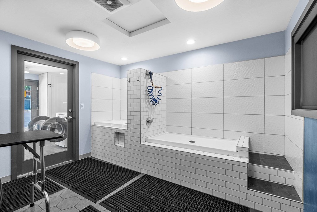 A bathroom with a white tiled shower area and a black mat on the floor.