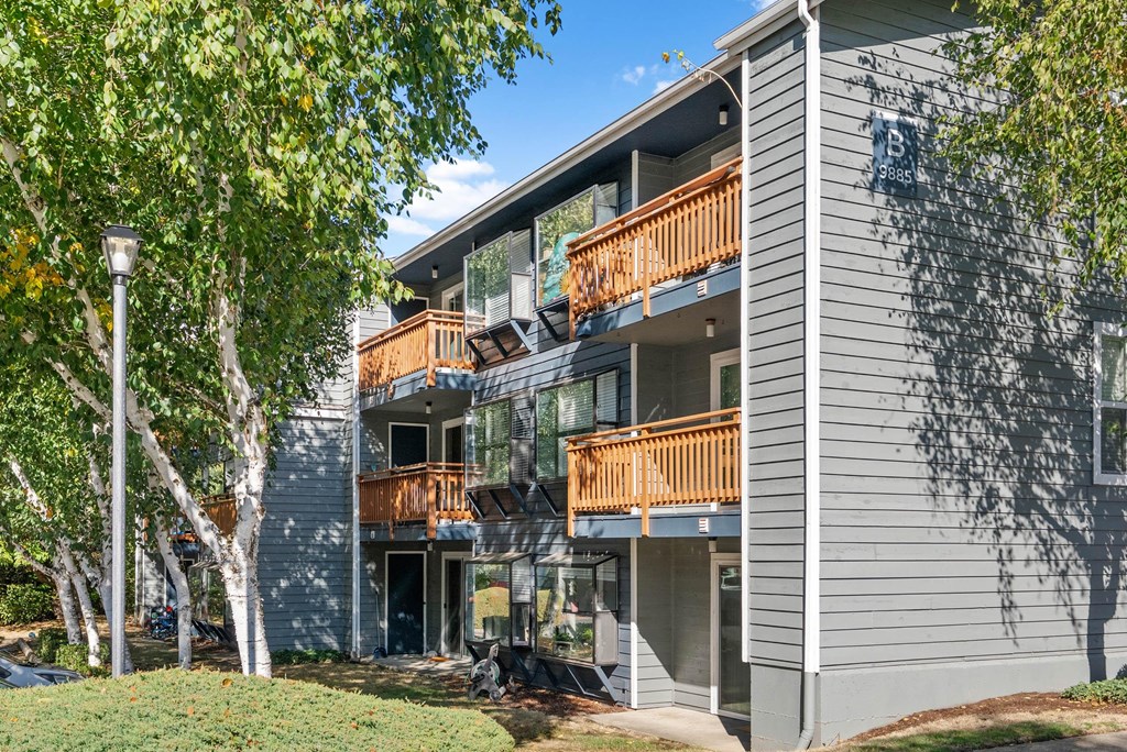 A grey building with a balcony and trees in front.