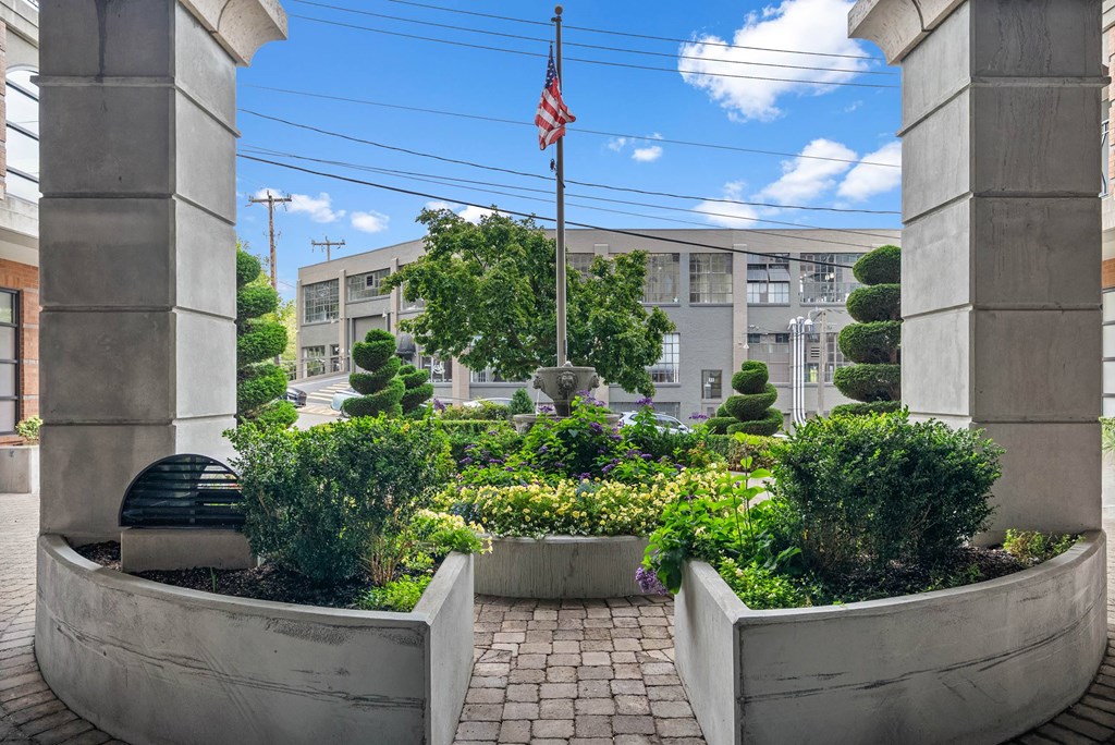 A garden with a flag on a pole is framed by two concrete pillars.