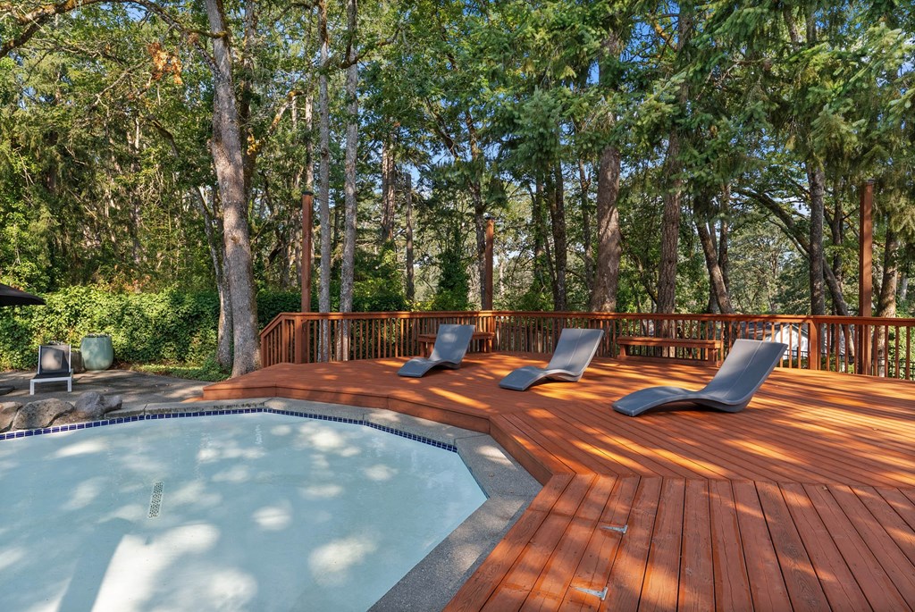 A wooden deck with a hot tub and lounge chairs.