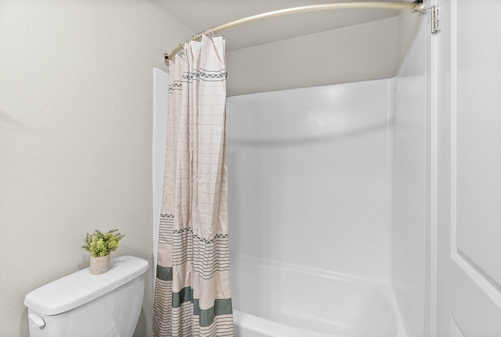 A white toilet sits next to a shower curtain in a bathroom.