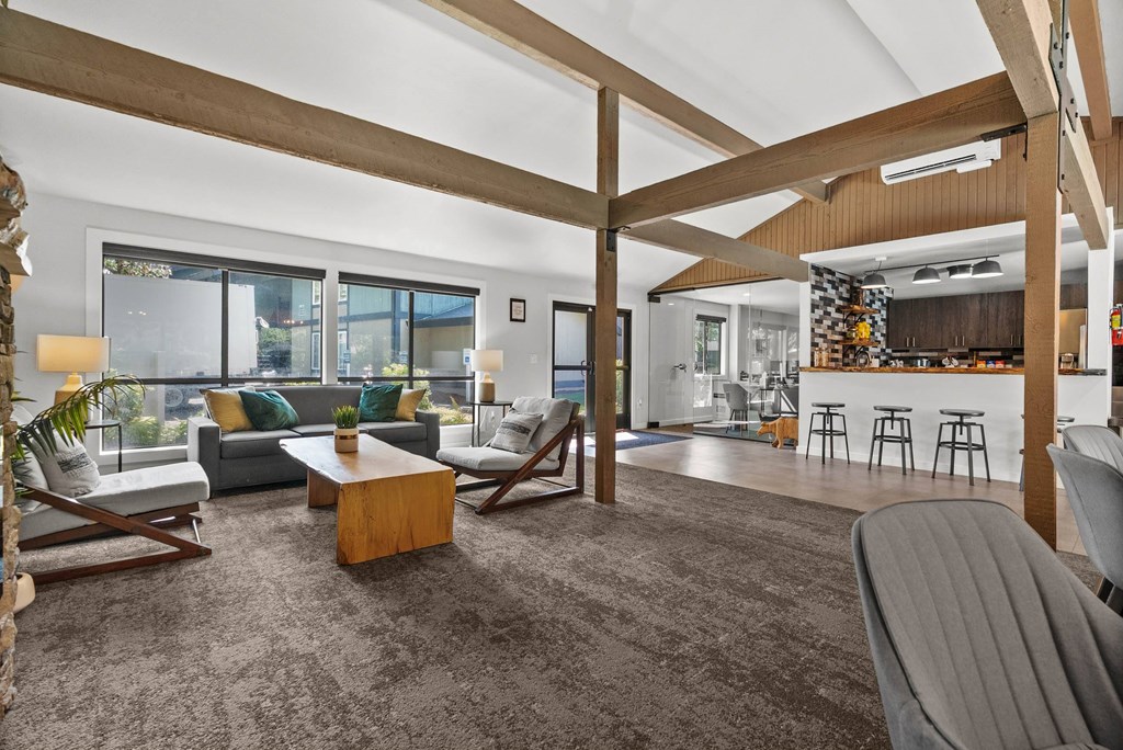 A living room with a grey carpet and wooden beams on the ceiling.