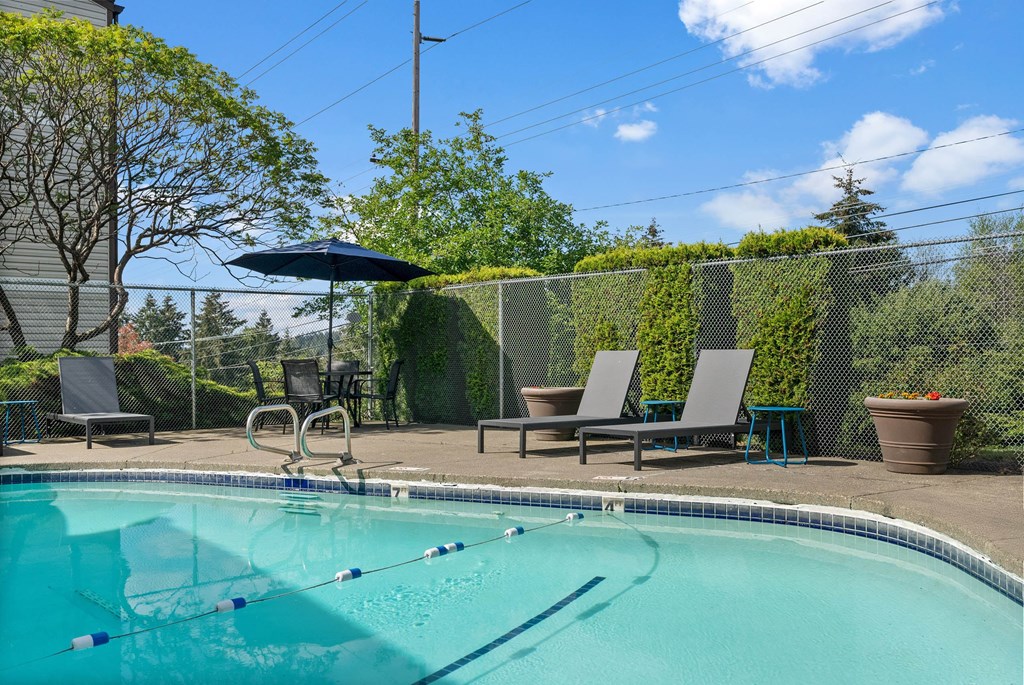 A pool with a diving board and lounge chairs.