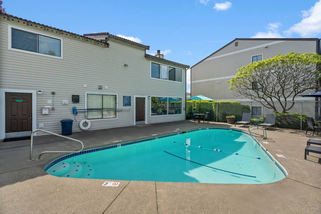 A swimming pool in front of a building with a tree to the right.