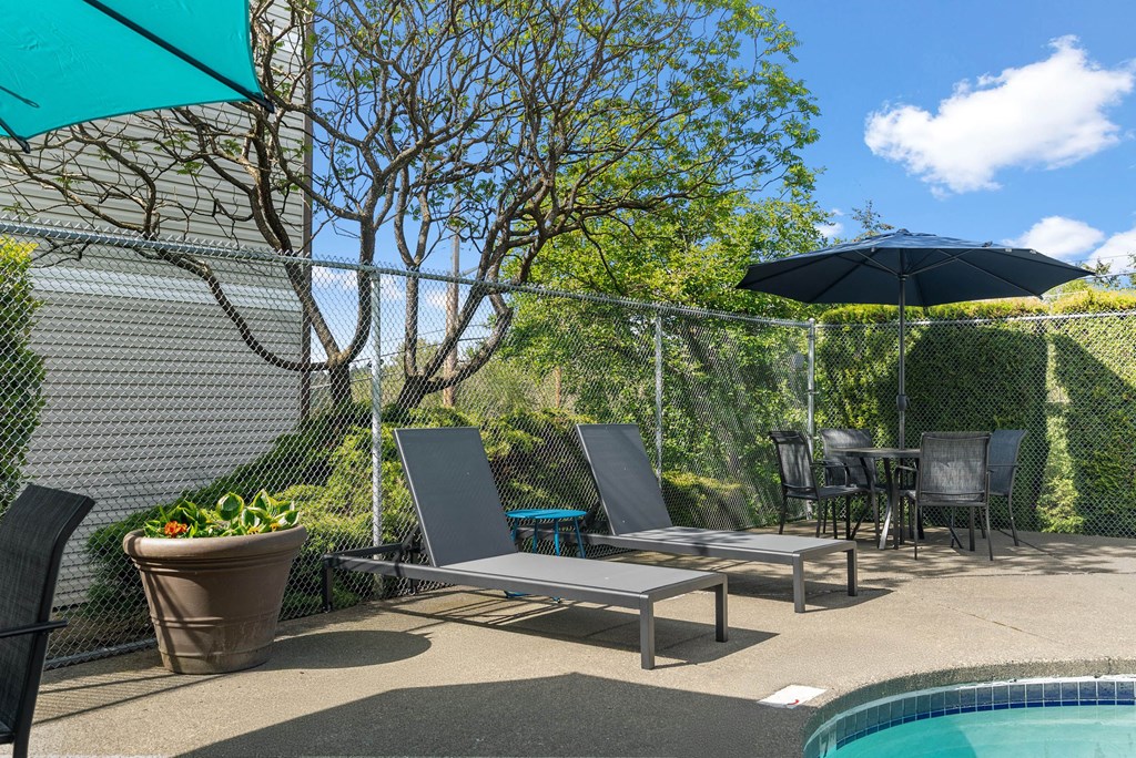 A poolside patio with a table, chairs, and a pool.