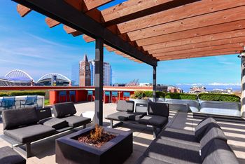 a roof deck with lounge chairs and a fire pit overlooking the city at Icon Apartments, Seattle, WA, 98104
