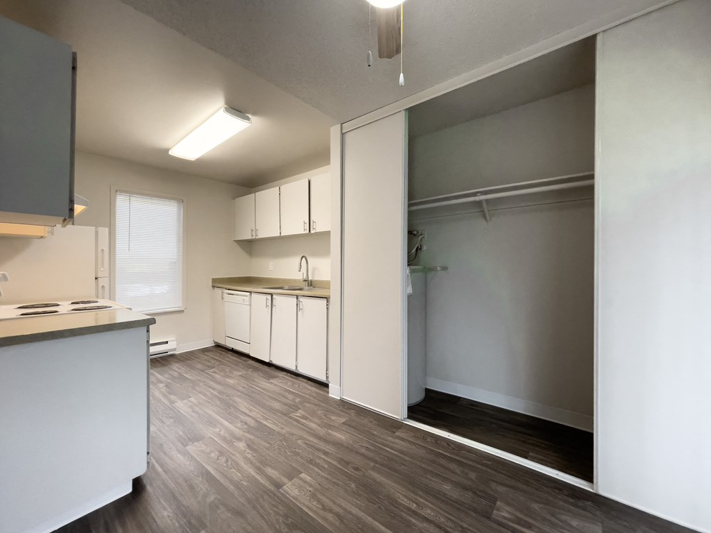 an empty living room and kitchen with white cabinets and wood flooring