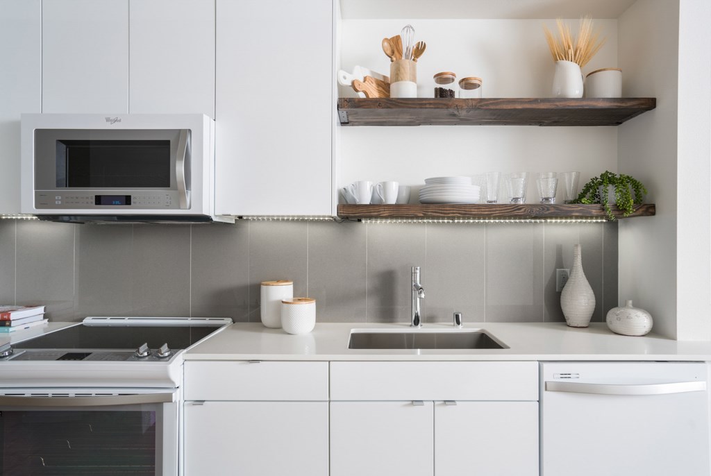 A white kitchen with a microwave above the stove and a sink below a shelf.
