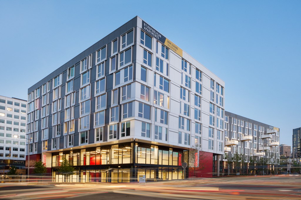 A modern multi-story building with a glass facade and a red entrance.