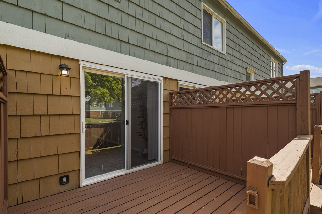 A wooden deck with a sliding glass door leading to a backyard.