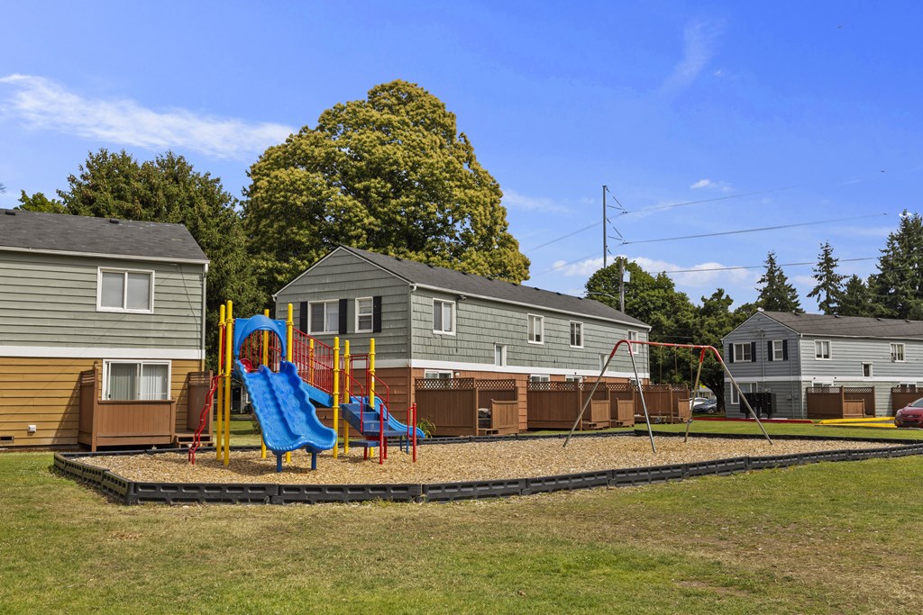 A playground with a blue slide and a red swing set in front of a row of houses.
