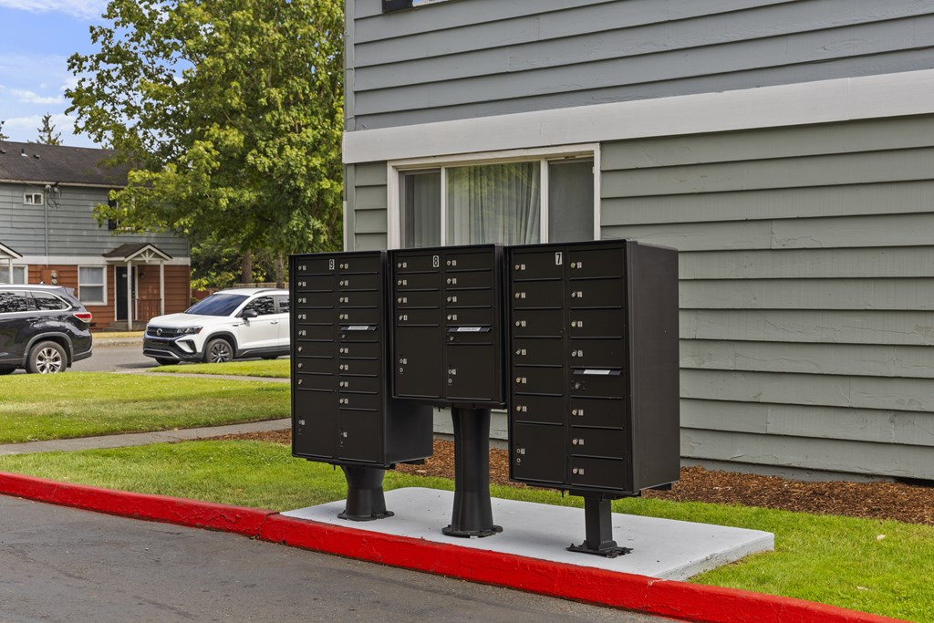 Two black mailboxes stand on a red curb in front of a house.