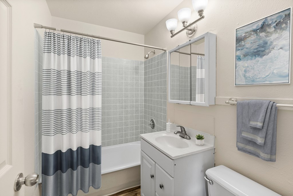 A bathroom with a white sink, a white toilet, a white bathtub, a white cabinet, a white shower curtain, a white tiled wall, a white door, a white light fixture, a white to