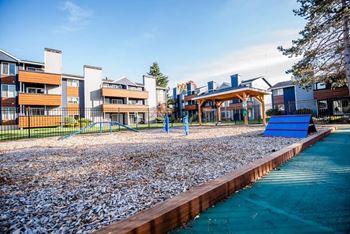 A playground with a blue slide and a pebble-covered area in front of apartment buildings. at Northpoint Apartments, Tacoma, WA