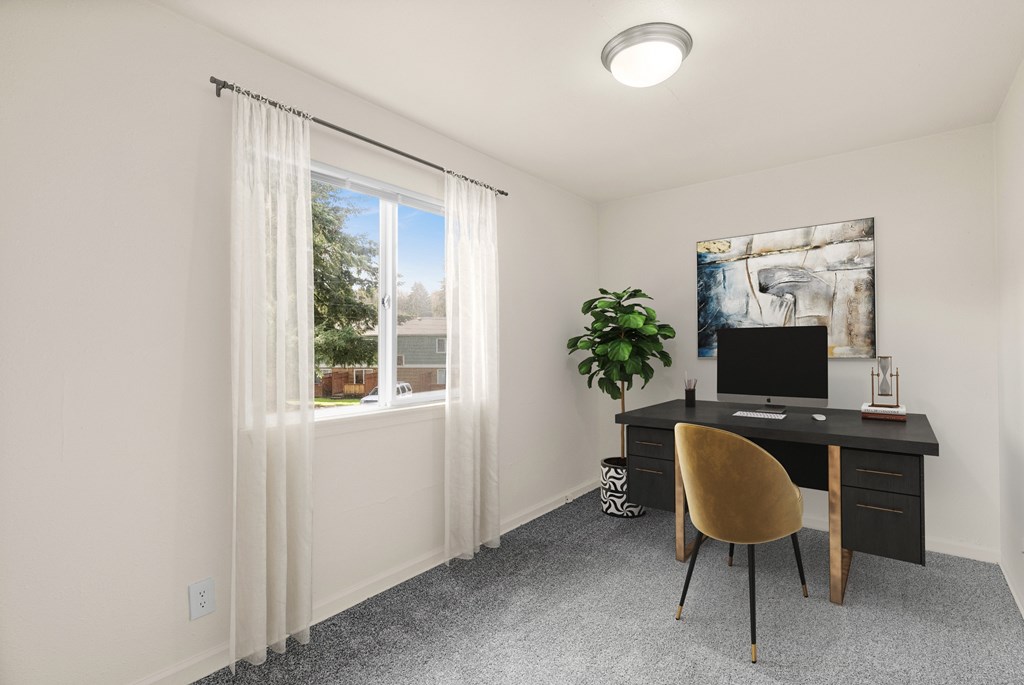 A room with a desk, chair, and a window with curtains.