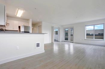 an empty living room with a kitchen and a large window