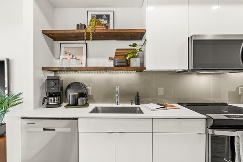 A modern kitchen with white cabinets and a wooden shelf above the sink.