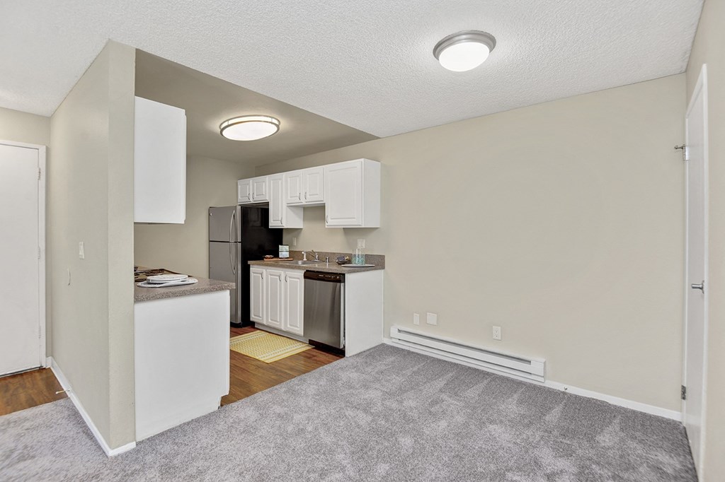 a living room with a kitchen in the background and a carpeted floor in the foreground