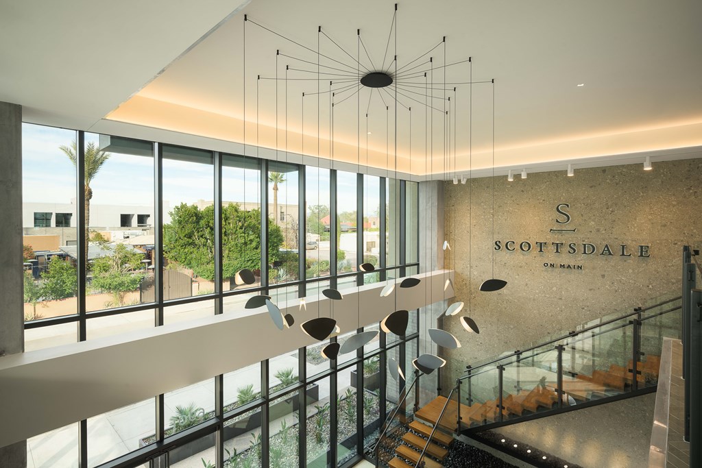 A modern interior of a building with a glass staircase and a hanging light fixture.