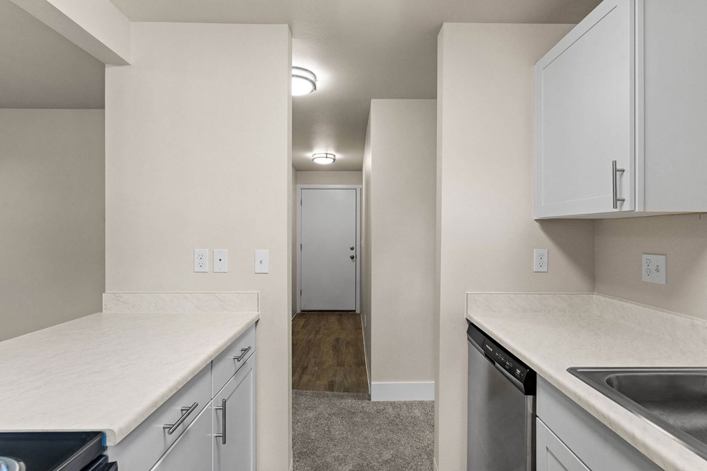 an empty kitchen with white countertops and white cabinets and a door to a hallway at Bellamy Park Apartments , Washington